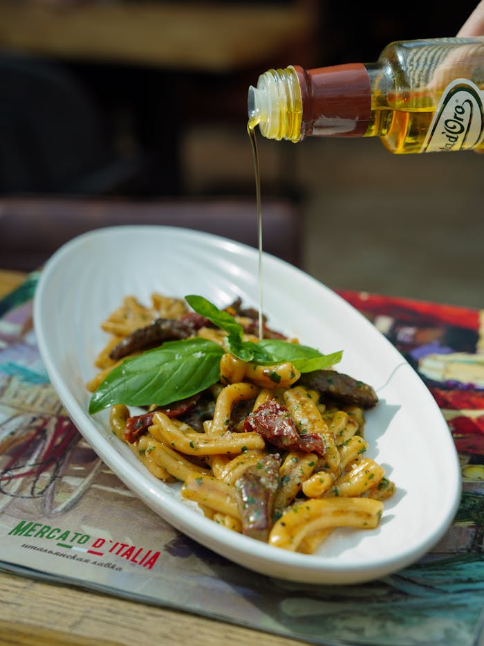 Close-up of a flavorful Italian pasta dish with olive oil being poured, highlighting fresh ingredients.