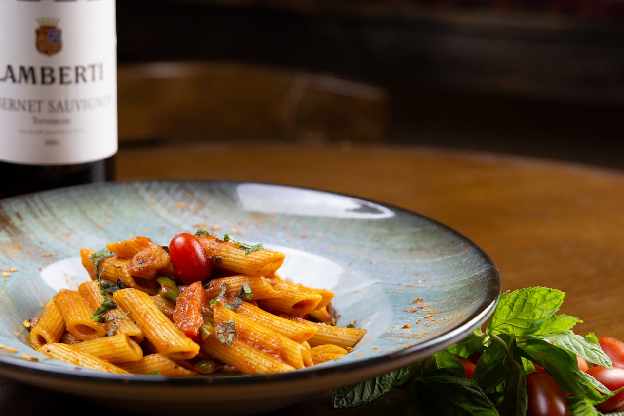 A vibrant plate of Italian penne pasta with tomato, basil, and paired wine.