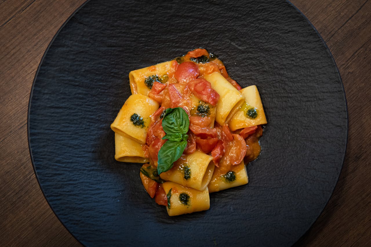 Top view of delicious Italian pasta with tomatoes and basil on a rustic black plate.